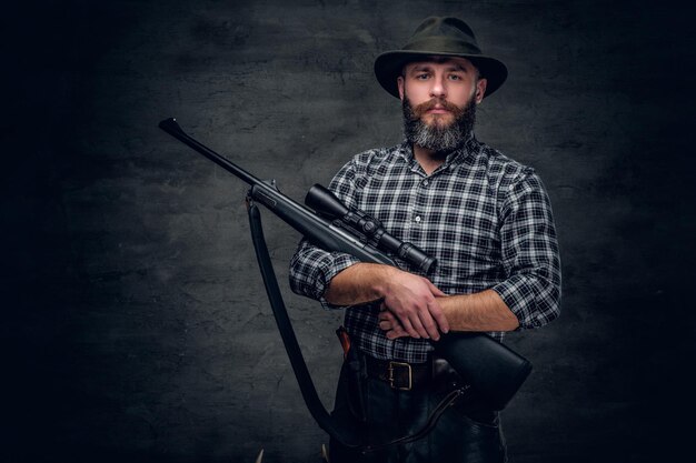 Studio portrait of a bearded hunter holds a rifle.