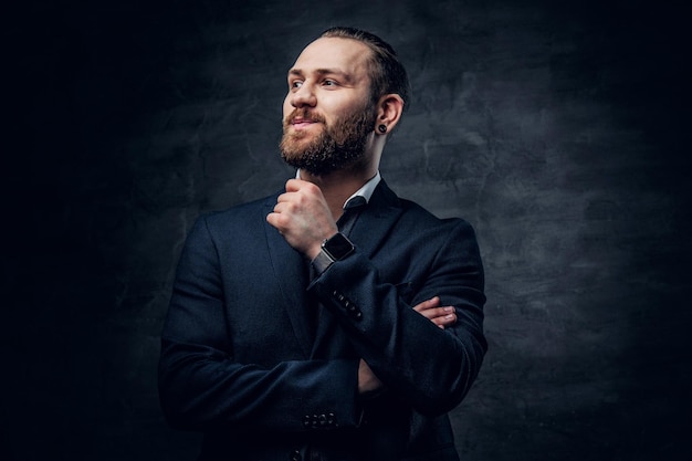 Studio portrait of bearded male dressed in a blue jacket over grey vignette background.