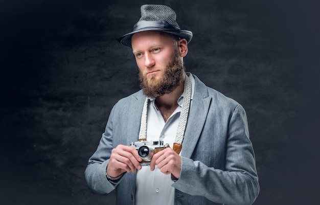 Free photo studio portrait of bearded photographer dressed a suit and felt hat  holds an old vintage slr photo camera.