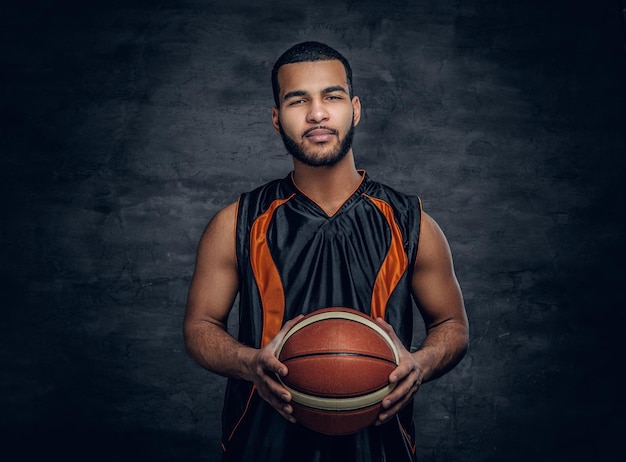 Free photo studio portrait of black basketball player holds a ball over grey background.