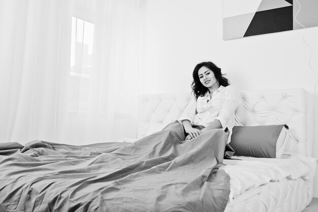 Studio portrait of brunette girl in white blouse lying on bed