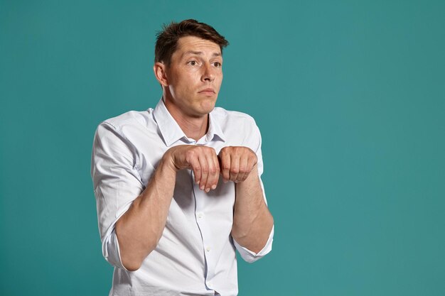 Studio portrait of a good-looking young guy in a classic white shirt act like he is a puppy while posing over a blue background. Stylish haircut. Sincere emotions concept. Copy space.