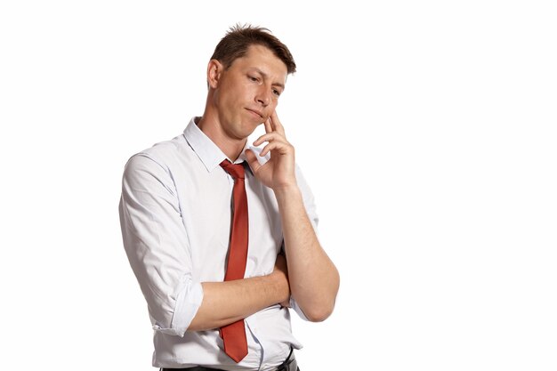 Studio portrait of a handsome young man in a classic white shirt and red tie looking thoughtful while posing isolated on white background. Stylish haircut. Sincere emotions concept. Copy space.