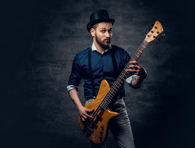 Studio portrait of the hipster bass player dressed in cylinder hat.