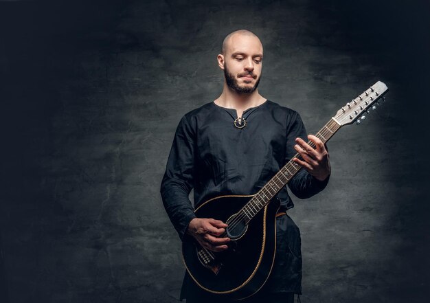 Studio portrait of a man in traditional Celtic clothes playing on mandolin over grey vignette background.