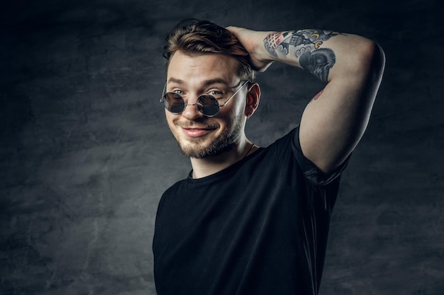 Free photo studio portrait of positive hipster male with tattoos on his arms over grey vignette background.