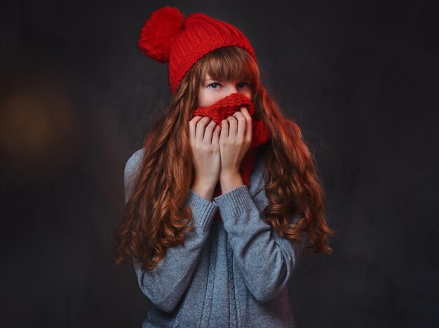 Studio portrait of redhead female in a warm clothes posing over grey background.