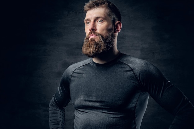 Studio portrait of sporty bearded male dressed in a grey sportswear over dark grey background.