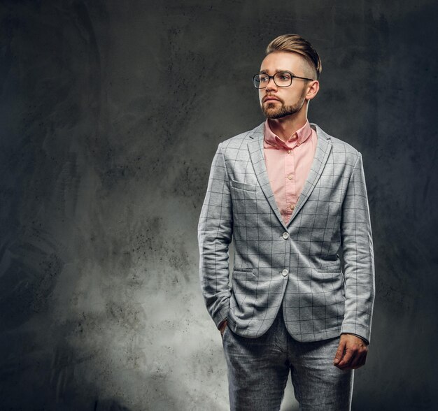 Studio shoot of styilish attractive man in checkered suit, glasses and pink shirt. He put one hand to his pocket.