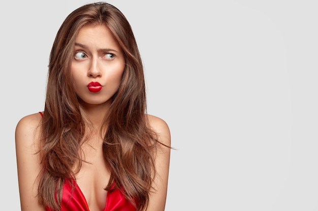 Studio shot of beautiful brunette young woman posing against the white wall