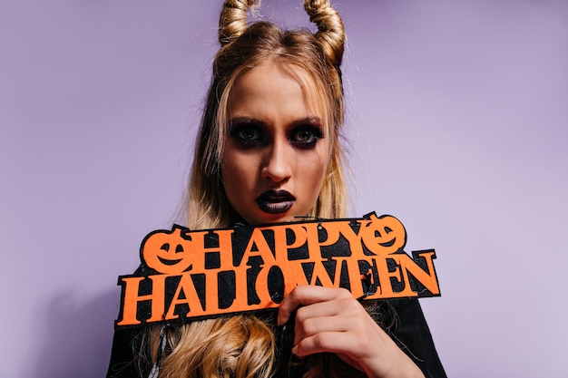 Studio shot of blonde witch isolated on purple background Adorable woman celebrating halloween alone