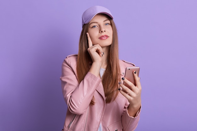 Studio shot of charming lady looking directly at camera while holding smart phone in hands