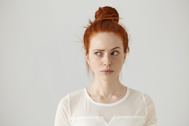 Free photo studio shot of cute redhead girl with hair knot and freckles looking sideways