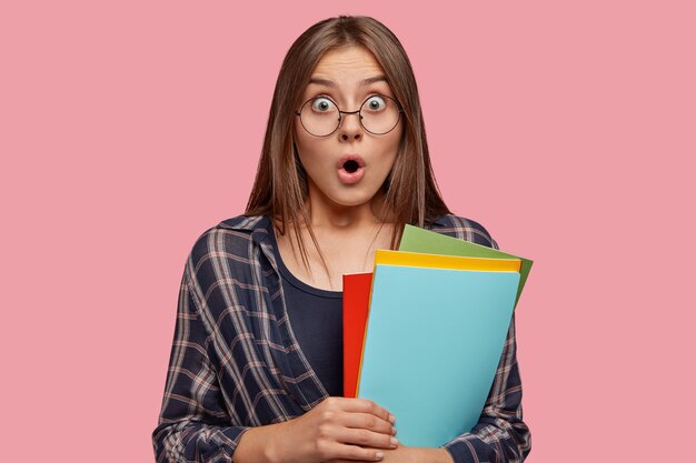 Studio shot of emotional young Caucasian woman with bugged eyes, opens mouth from amazement