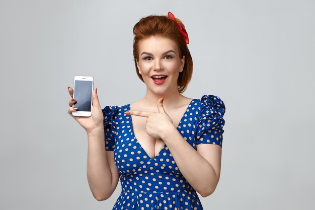 Studio shot of euphoric positive young housewife wearing retro dress and hairstyle exclaiming emotionally,