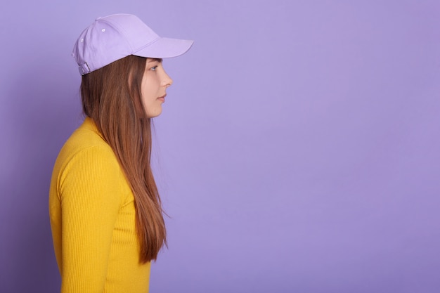 Free photo studio shot of female wearing baseball cap and yellow shirt, side view of attractive female looking straight ahead