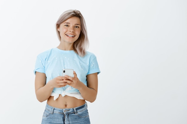 Free photo studio shot of good-looking blonde girl posing with her phone in the studio