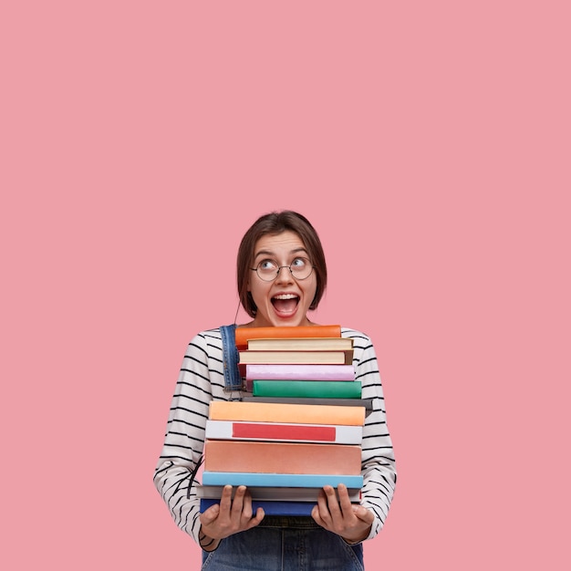 Free Photo studio shot of joyful european woman wears round spectacles, holds many books