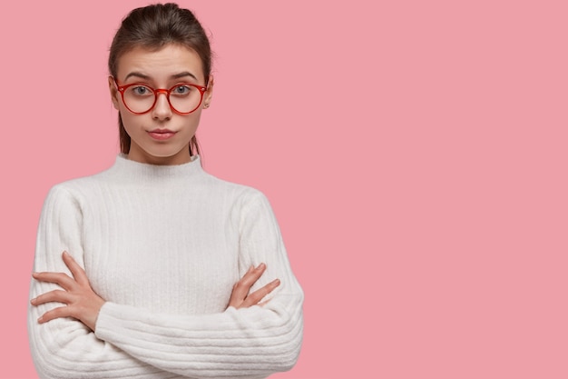 Free photo studio shot of pretty woman looks with attentive facial expression, keeps hands crossed, wears jumper