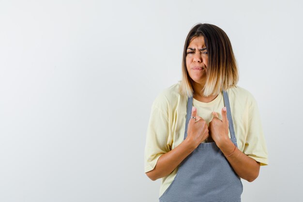 Studio shot of sad mexican woman in light yellow t-shirt and check apron shows herself sadly isolated on white background