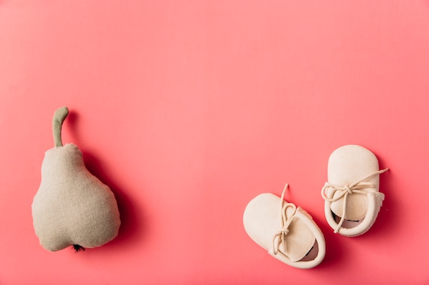 Free photo stuffed pear fruit and pair of baby's shoes on colored background