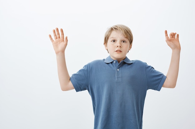 Free photo stunned afraid cute boy with blond head, raising palms in surrender, holding breath and staring scared, being caught near fridge at night