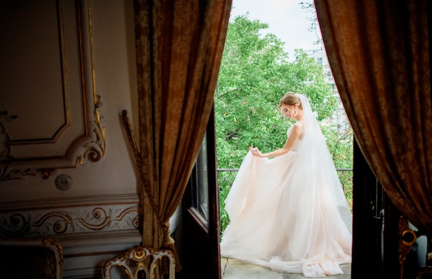 Free photo stunning bride in a wedding dress poses on the balcony in a luxury hotel room