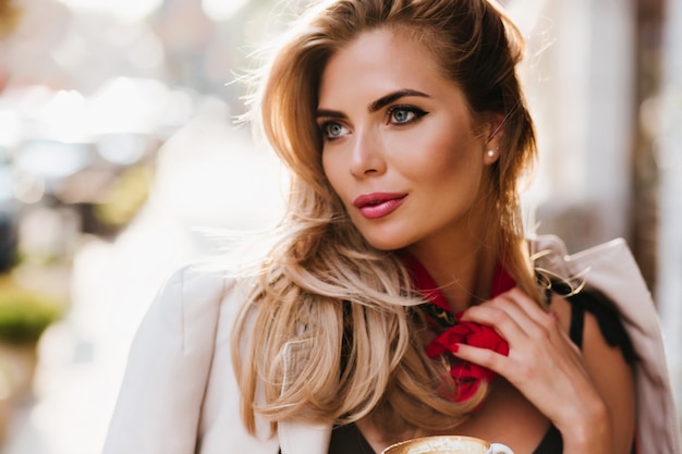 Free photo stunning european girl with glamorous make-up looking away touching her red scarf. close-up portrait of beautiful fair-haired woman with blue eyes relaxing