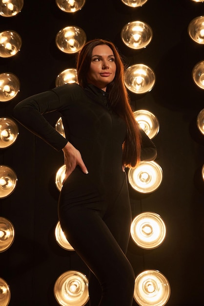 Free Photo stunning lady wearing dark apparel posing with hand on waist in black studio front view of caucasian