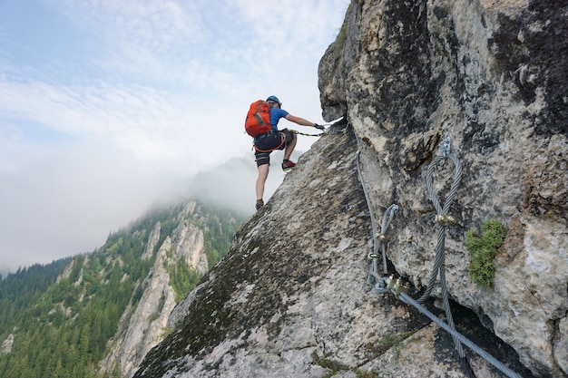 Stunning shot of a young man climbing up a cliff on a cold and foggy day