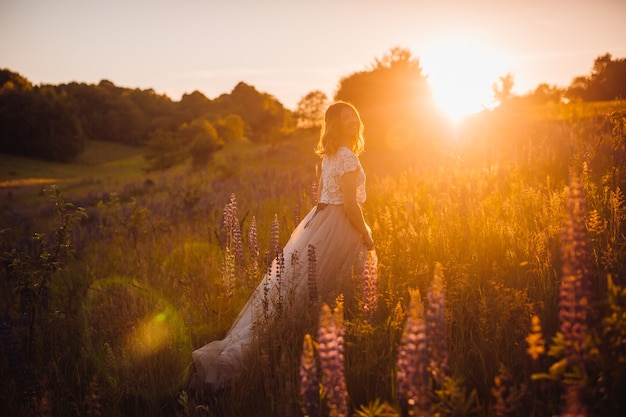 Free photo stunning woman in bright dress walks across the field in the rays of sunset