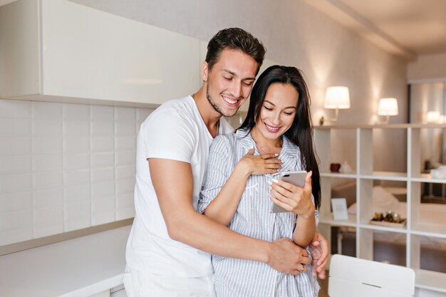 Stunning woman with surprised smile reading phone message while husband embracing her