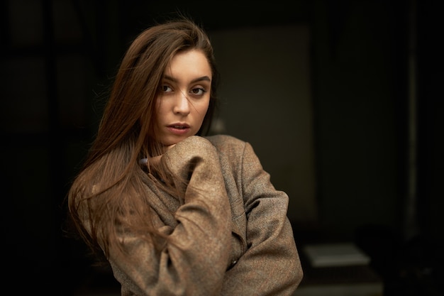 Free photo style, fashion, beauty and femininity concept. adorable gorgeous young woman with loose brown hair looking at camera with serious confident facial expression, dressed in oversize jacket or coat