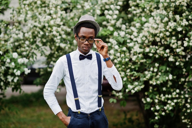 Stylish african american business man at pants with suspender and shirt with bow tie hat and glasses posed outdoor