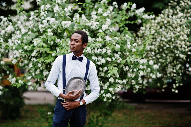 Stylish african american business man at pants with suspender and shirt with bow tie hat posed outdoor