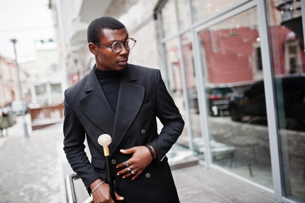 Stylish african american gentleman in elegant black jacket holding retro walking stick as cane flask or tippling cane with golden diamond ball handle Rich fashionable afro man