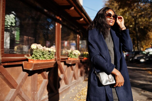 Stylish african american girl in blue coat and sunglasses posed at sunny autumn day Africa model woman