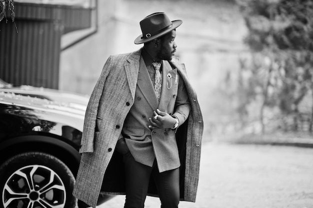 Free photo stylish african american man model in gray coat jacket tie and red hat against black suv car black and white photo