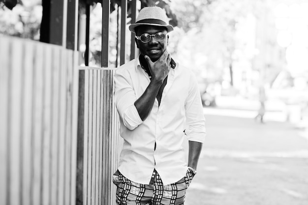 Stylish african american man in white shirt and colored pants with hat and glasses posed outdoor Black fashionable model boy