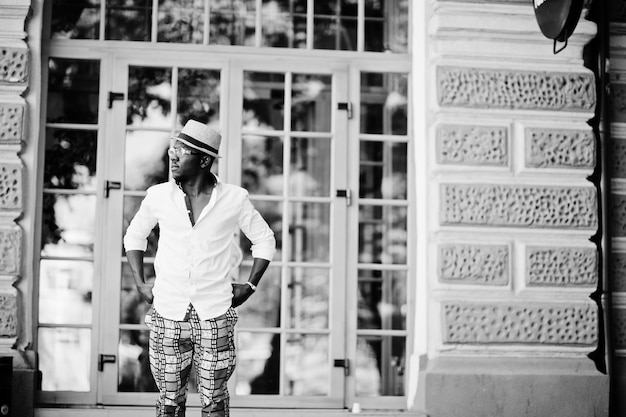 Stylish african american man in white shirt and colored pants with hat and glasses posed outdoor Black fashionable model boy