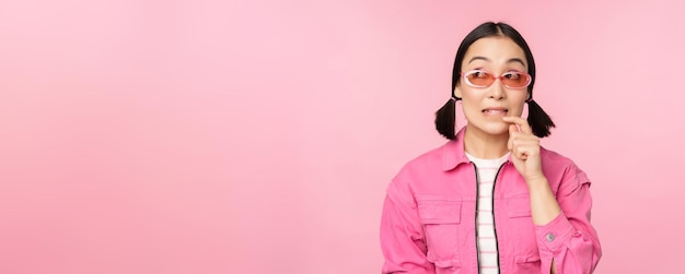 Stylish asian girl in sunglasses looks thoughtful or intrigued wants to try smth out stands over pin