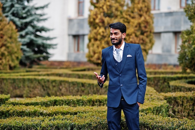 Free photo stylish beard indian man with bindi on forehead wear on blue suit posed outdoor against green bushes at park