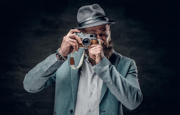 Free Photo a stylish bearded hipster male dressed in a grey jacket and felt hat holds an slr photo camera.