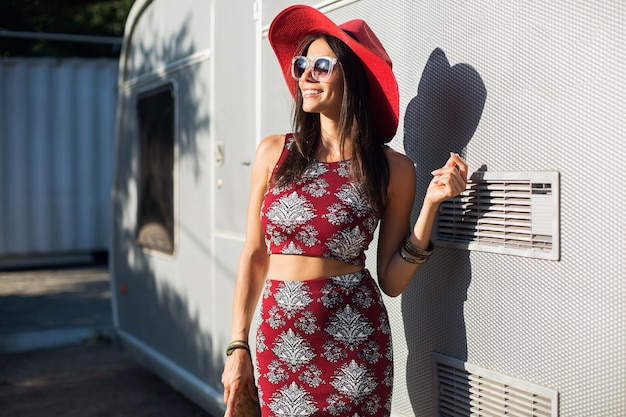 Stylish beautiful woman posing against silver trailer in tropical style outfit