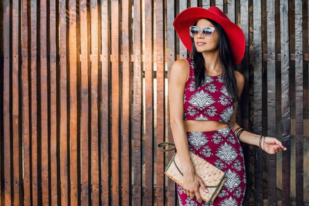 Stylish beautiful woman posing against wooden wall in tropical style outfit