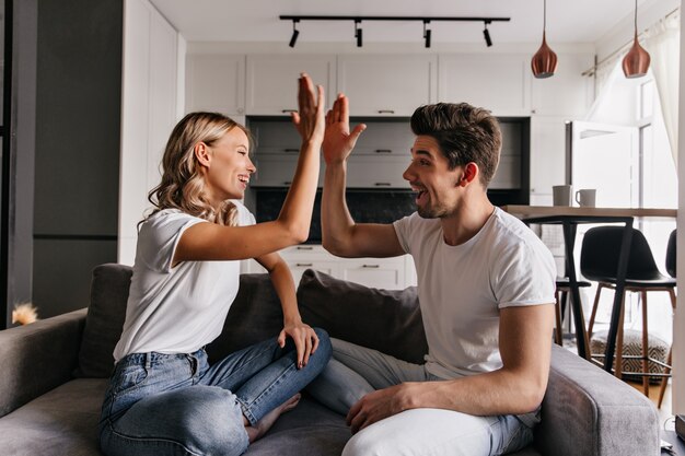 Stylish blonde girl playing with boyfriend in living room. Indoor portrait of joking young people.