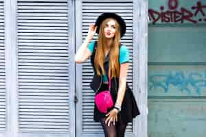 Free photo stylish blonde woman posing on the street, wearing hipster bright outfit, playful cool emotions, fun, enjoy, happy vacation alone, vintage hat and mini skirt.