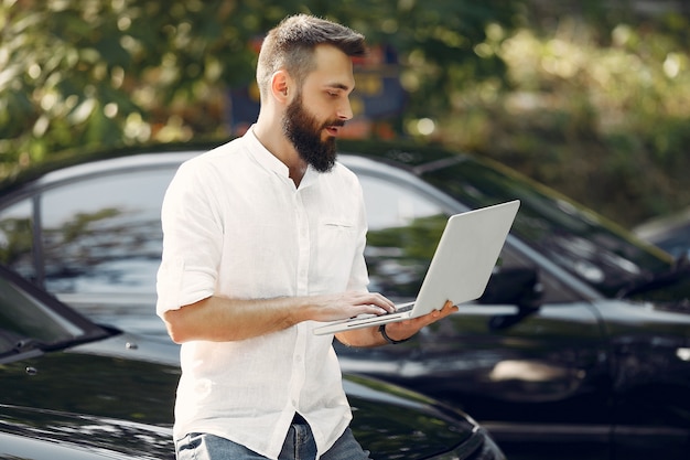 Stylish businessman standing near the car and use the laptop