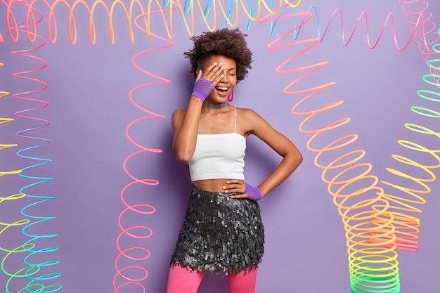 Free Photo stylish carefree woman makes face palm, wears cropped top and glittering skirt, laughs happily, has fun in merry company