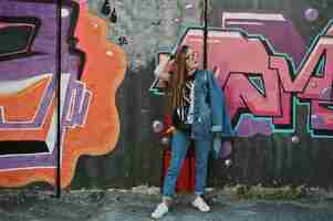 Free photo stylish casual hipster girl in jeans wear and glasses against large graffiti wall